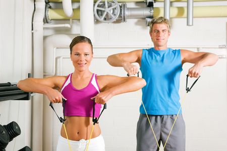 Very fit couple in a gym exercising with tube equipment doing power gymnastics