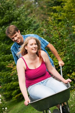 Man carrying his girl in a wheelbarrow through their gardenの写真素材