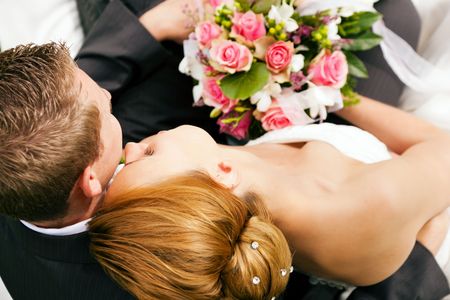 wedding couple hugging and kissing, the bride holding a bouquet of flowers in her handの写真素材
