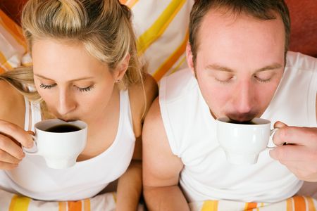 Couple having breakfast in bed in the morning enjoying their coffeeの写真素材