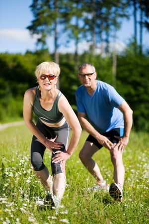 Mature or senior couple in jogging gear doing sport and physical exercise outdoors, stretching and gymnasticsの写真素材