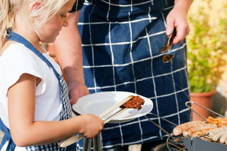 Father and daughter preparing meat and sausages using a barbecue grillの写真素材