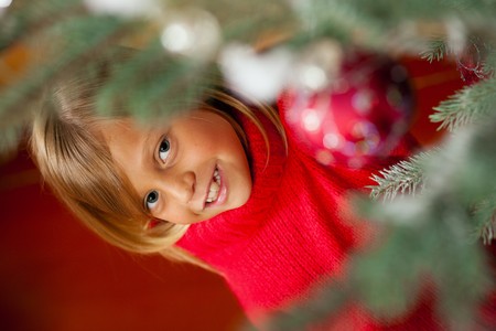 Young girl helping decorating the Christmas tree, holding some Christmas baubles in her hand (Focus on girl)の写真素材