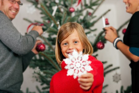 Young girl helping her family decorating the Christmas tree, holding a Christmas Snowflake in her handの写真素材