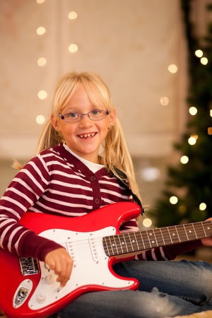 Young child with her guitar - presumably a present - in front of a Christmas treeの写真素材