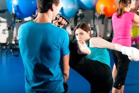 Woman Kick boxer kicking her trainer in a sparring session, in the background other boxers are...
