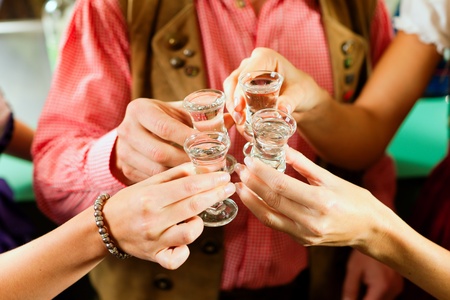 People in Bavarian Tracht clinking glasses with hard liquor in a pubの写真素材