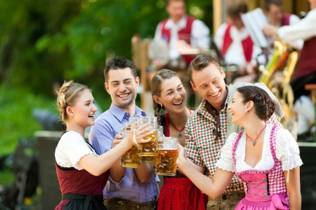 In Beer garden in Bavaria, Germany - friends in Tracht, Dirndl and Lederhosen and Dirndl standing in front of bandの写真素材