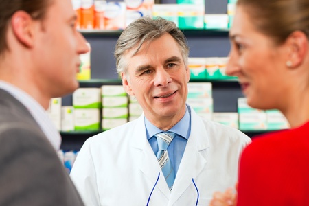 Pharmacist is consulting customers in his pharmacy - a man and a womanの写真素材