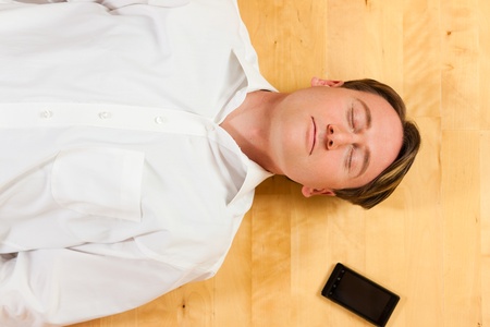 Man lying with closed eyes on the floor at home, a telephone beside himの写真素材