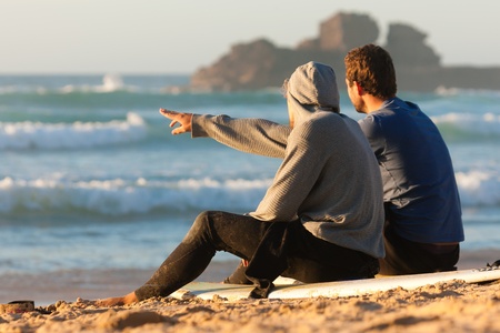 Two surfers sitting on their surf boards on the beach discussing the wavesの写真素材