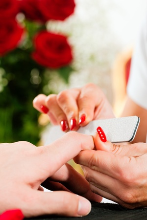 Man in a nail salon receiving a manicure by a beautician, lots of roses in the backgroundの写真素材