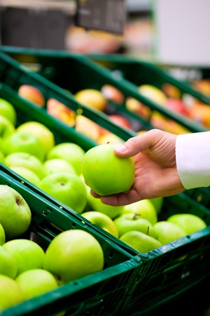 Man â only hand to be seen -  in a supermarket at the shelf for fruits shopping for groceries, he is checking out the applesの写真素材