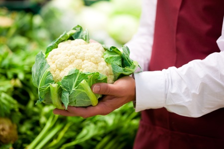 Man â only hands to be seen - in supermarket as shop assistant; he is carrying a cauliflower  の写真素材