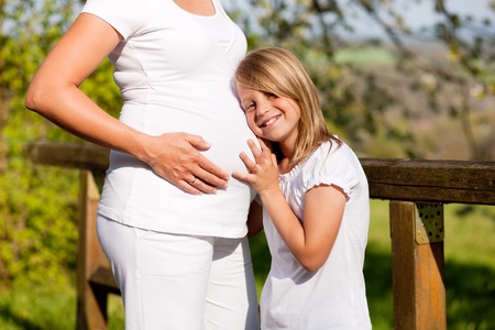 Family affairs - Girl is touching round belly of her pregnant mother in eager anticipation of the new child の写真素材