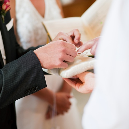 Couple having their wedding ceremony in church in front of a catholic priest, groom taking the ring to give it to the brideの写真素材