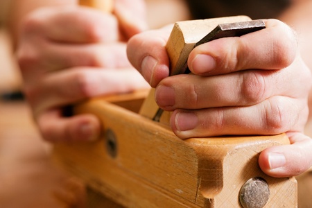 Carpenter working with a planer in his workshop, close-up on the tool with hands 
