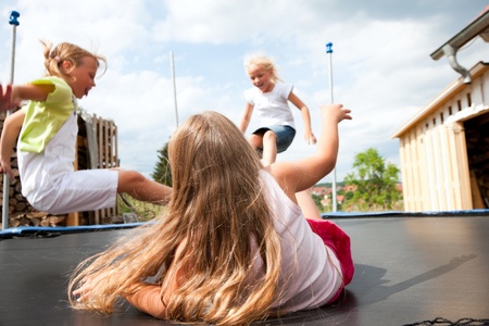 Three children jumping on a trampoline in front of their homeの写真素材
