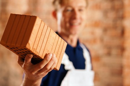 Bricklayer with brick at a construction site, focus is on the brick!の写真素材