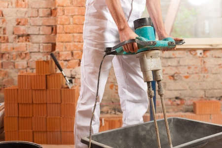 Construction worker mixing concrete or grout with a hand mixerの写真素材