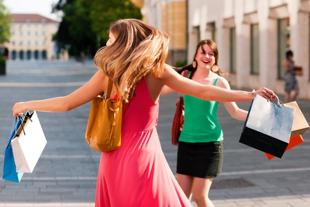 Two women being friends shopping downtown with colorful shopping bags, they are jumping for joy  の写真素材