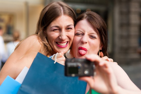 Two woman being friends shopping downtown with colourful shopping bags and taking a picture from themselves の写真素材