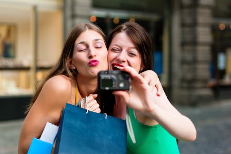 Two woman being friends shopping downtown with colourful shopping bags and taking a picture from themselves の写真素材