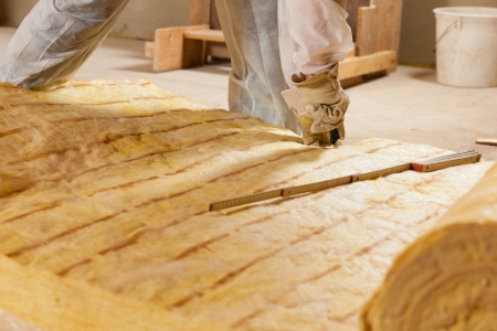 Man - only hand to be seen - cutting some glass wool as material for thermal insulation of a new...