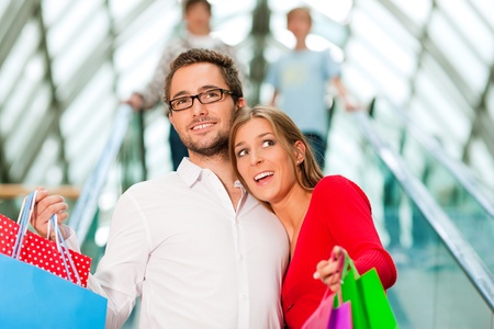 Couple - man and woman - in a shopping mall with colorful bags on an escalatorの写真素材