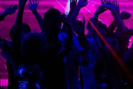 Silhouettes of dancing people having a celebration in a disco club, the light show is sending laser beams through the backlit sceneの写真素材