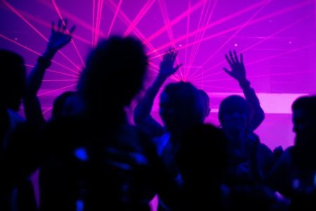 Silhouettes of dancing people having a celebration in a disco club, the light show is sending laser beams through the backlit sceneの写真素材