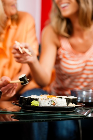 Mother and adult daughter eating sushi at home - FOCUS is on the sushi plateの写真素材