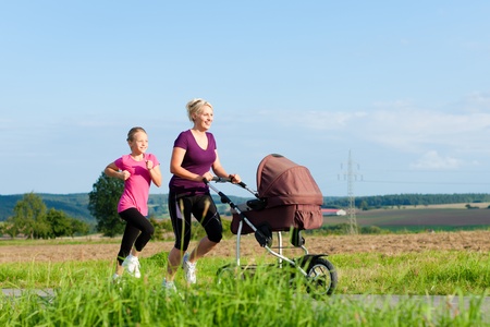Family sport - mother and daughter jogging down a path with a baby stroller at a wonderful sunny dayの写真素材