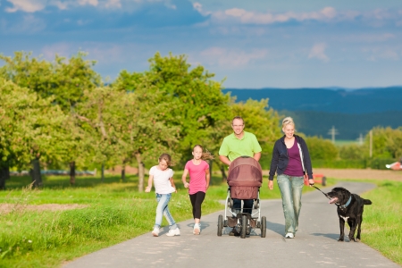 Family with three children (one baby lying in a baby buggy) walking down a path outdoors, there is also a dogの写真素材