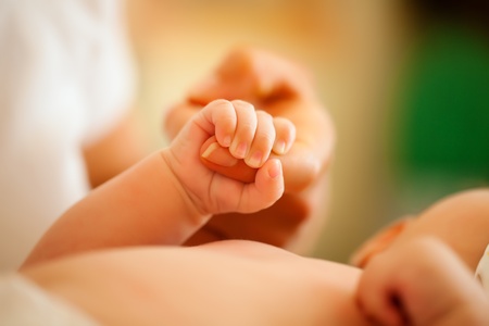 Baby grabbing the hand of her mother who is taking care of her (Focus is on hand)の写真素材