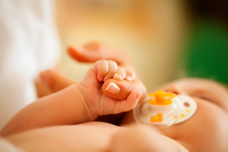 Baby grabbing the hand of her mother who is taking care of her (Focus is on hand)