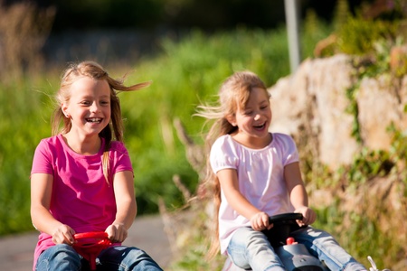Two sisters with toy cars driving them down a hill having awesome amounts of funの写真素材