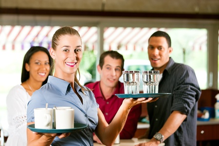 Woman as waitress in a bar or restaurant with coffee mugs; in the background are guestsの写真素材