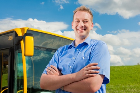 Bus driver is standing in front of his bus under al blue sky