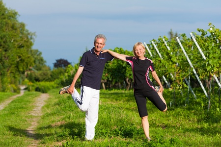 Mature or senior couple in jogging gear doing sport and physical exercise outdoors in a vineyard, stretching and gymnasticsの写真素材