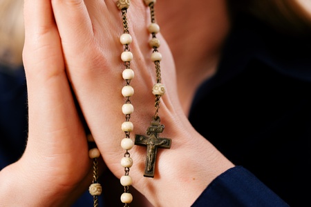 Woman (only close-up of hands to be seen) with rosary sending a prayer to God, the dark setting suggests she is sad or lonely   の写真素材
