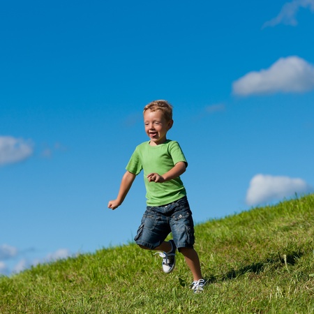 Little boy running down a meadow in a beautiful landscape in summer  の写真素材