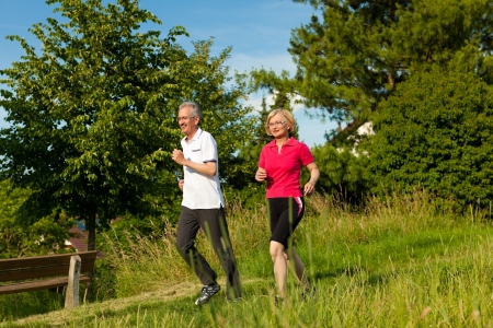 Mature or senior couple doing sport outdoors, jogging down a path in summerの写真素材
