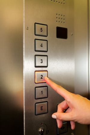 Woman in elevator or lift is pressing the button to get into the right floor; only hand to be seen -...