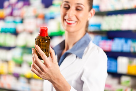 Female pharmacist is standing in her drugstore behind the counter and holds a medicine bottleの写真素材