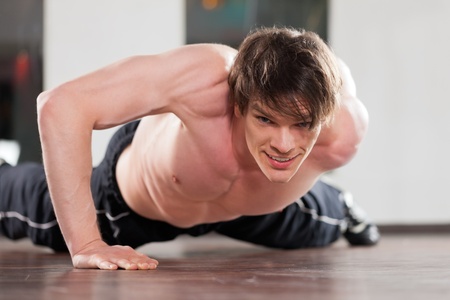 Muscular man exercising by doing pushups with only one arm in a gym  