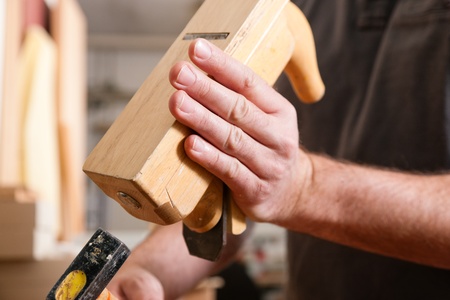 Carpenter working with a planer in his workshop, close up on the tool with hands 