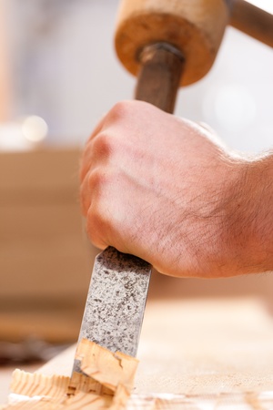 Carpenter working with a chisel and hammer in his workshop; close-up on chisel