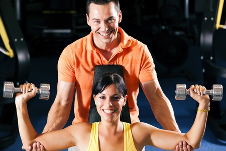 Woman with her personal fitness trainer in the gym exercising with dumbbellsの写真素材
