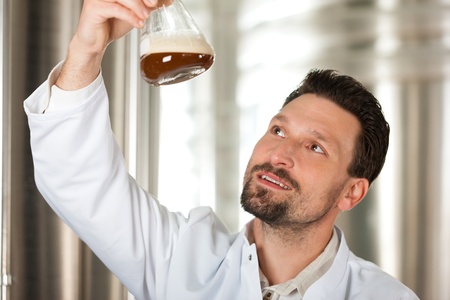 Brewer standing in his brewery and is examining the beer for its purity